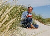 Krischan Koch sitz mit einem Buch in den Dünen