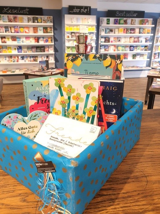 Geschenkebox mit Karten und Büchern vor einem Bücherregal