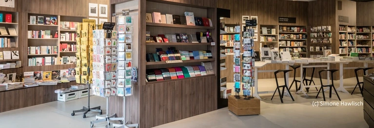Vorderer Bereich der Buchhandlung mit Postkartenständern und Regalen.
