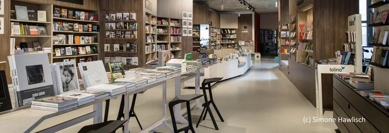 Ein Ausschnitt des Ladeninneren. Zu sehen ist ein langer Tisch mit Büchern darauf und Bücherregale.