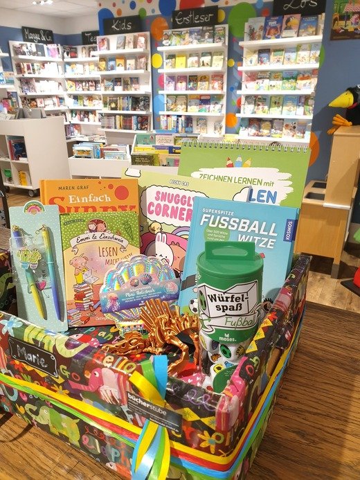 Geschenkebox mit Büchern und Spielen vor einem Bücherregal