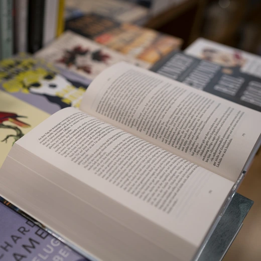 Ein Close Up eines aufgeschlagenen Buchs auf einem Tisch voller Bücher