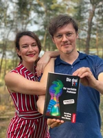 Cally Stronk & Christian Friedrich stehen in der Natur und halten gemeinsam ihr Buch hoch.